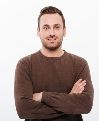 Image of handsome young cheerful man standing isolated over white background with arms crossed. Looking camera.