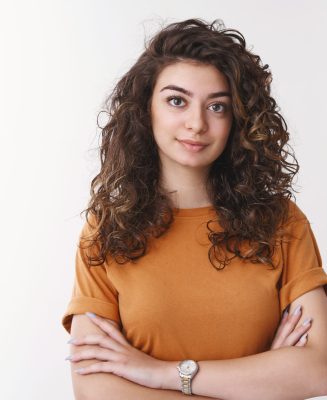 Young determined armenian curly-haired female university student listen carefully asignment look confident ready do task cross hands chest smiling self-assured, standing white background.